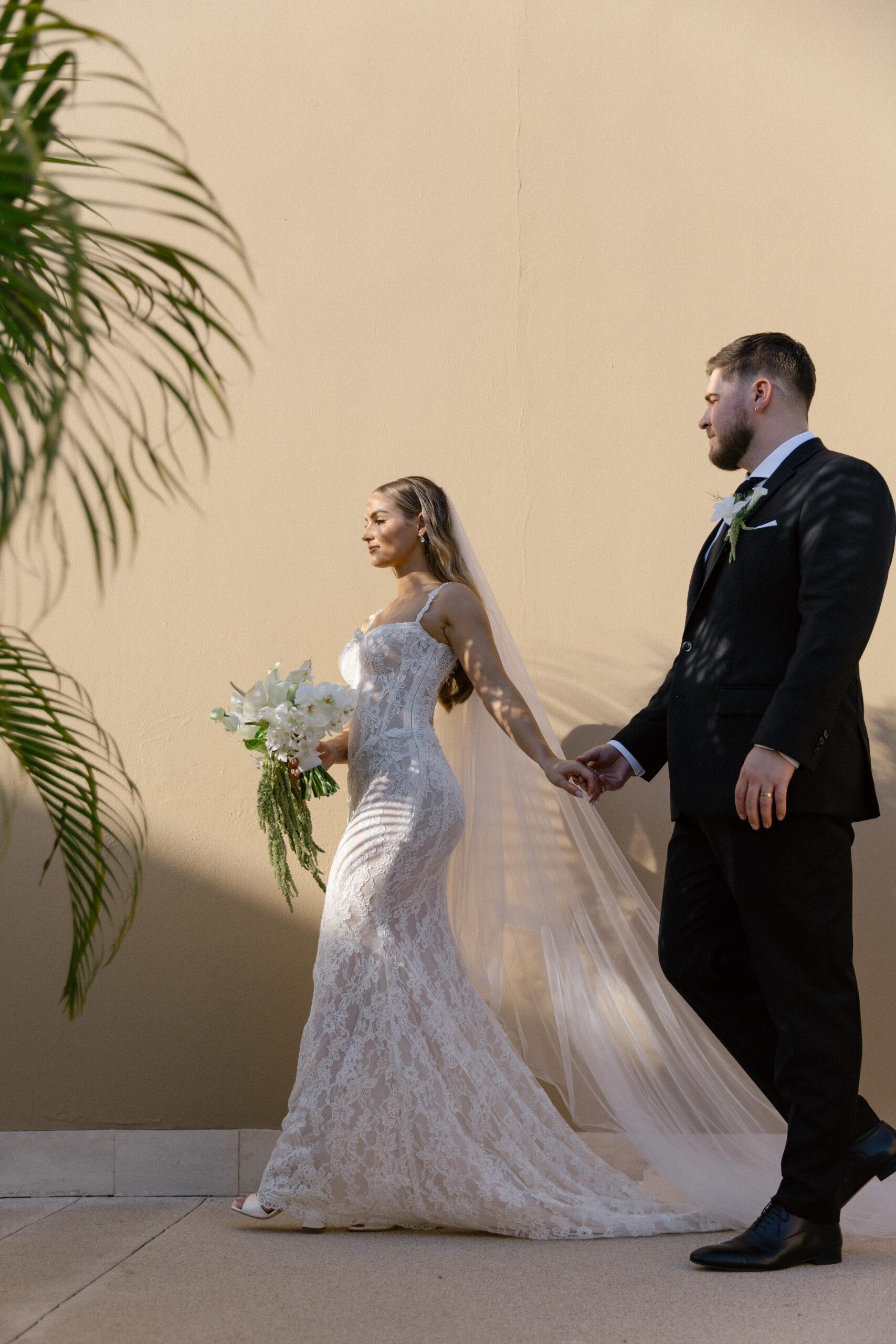 Bride and groom walking hand in hand along a neutral-toned wall at Montage Los Cabos wedding in Cabo San Lucas Mexico